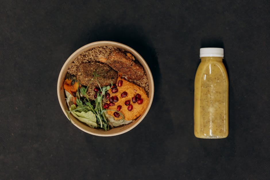 A vibrant vegan bowl with quinoa, fresh vegetables, and a smoothie bottle against a dark backdrop