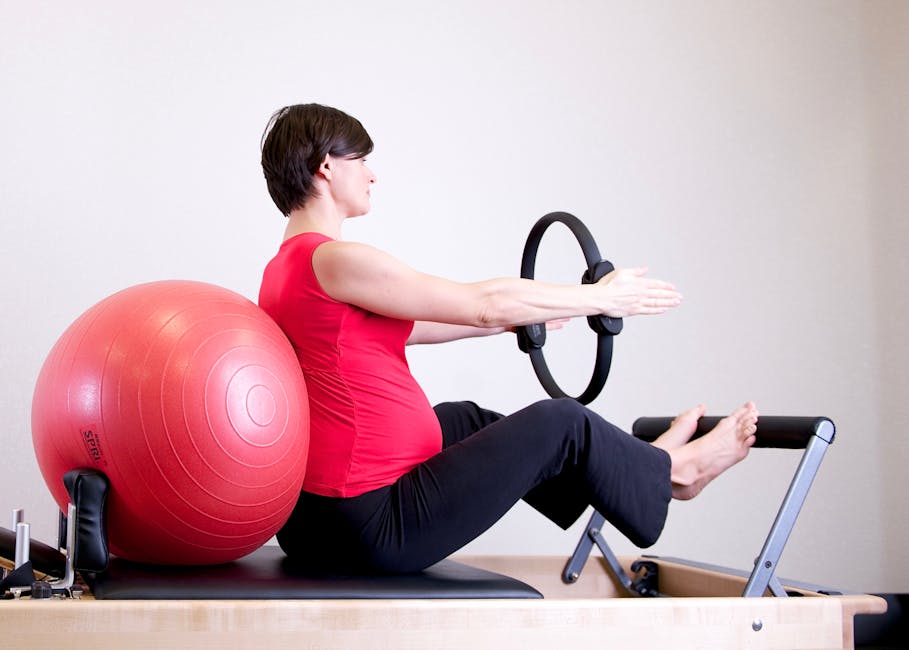 A pregnant woman in a red top practicing Pilates using a fitness ring
